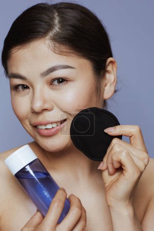 Téléchargez les photos : Jeune asiatique femelle avec démaquillant et coton noir pad sur fond bleu. - en image libre de droit