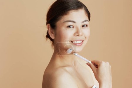 Foto de Retrato de mujer asiática moderna con masajeador de rodillos aislado sobre fondo beige. - Imagen libre de derechos
