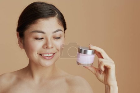 Foto de Mujer moderna con frasco de crema facial contra fondo beige. - Imagen libre de derechos