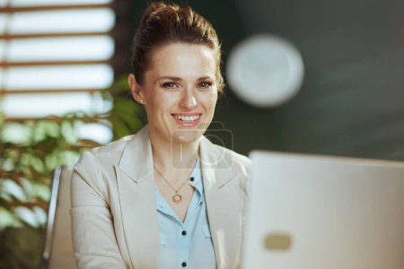 Foto de Retrato de mujer de negocios moderna feliz de 40 años en un traje de negocios ligero en la oficina verde moderna con el ordenador portátil. - Imagen libre de derechos