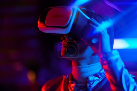 Téléchargez les photos : Neon metaverse concept futuriste. femme d'âge moyen à la mode en réalité virtuelle lunettes sur fond sombre. - en image libre de droit