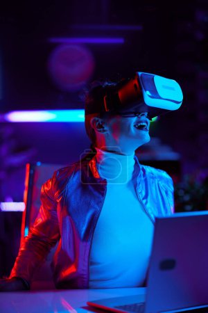 Foto de Concepto futurista neón metaverso. mujer moderna excitada en gafas de realidad virtual en la oficina moderna. - Imagen libre de derechos