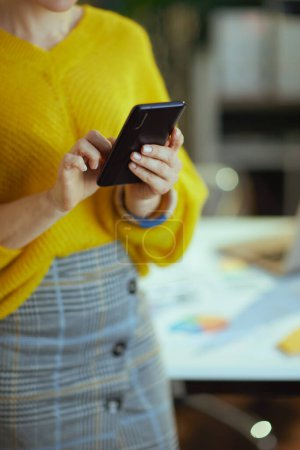 Téléchargez les photos : Gros plan sur propriétaire de petite entreprise femme en pull jaune dans le bureau vert en utilisant smartphone. - en image libre de droit