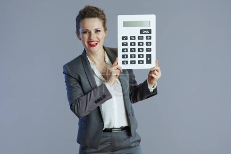 Photo for Happy trendy 40 years old small business owner woman in grey suit with calculator isolated on gray background. - Royalty Free Image