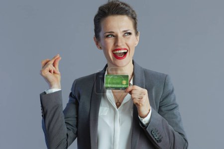 Foto de Sonriente elegante mujer de negocios de 40 años en traje gris con dedos de tarjeta de crédito haciendo clic aislado sobre fondo gris. - Imagen libre de derechos