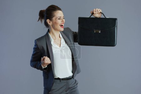 Photo for Happy stylish 40 years old woman employee in gray suit with briefcase against gray background. - Royalty Free Image