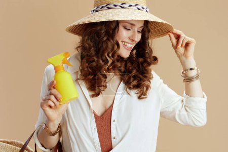 Photo for Beach vacation. smiling modern housewife in white blouse and shorts against beige background with sunscreen and summer hat. - Royalty Free Image