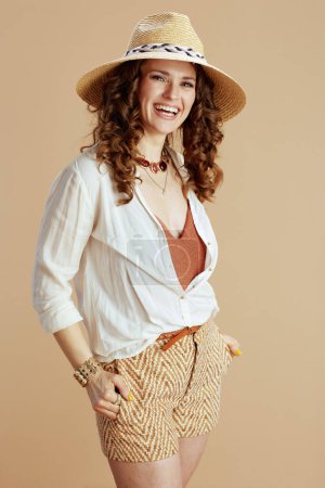 Téléchargez les photos : Vacances à la plage. femme souriante à la mode en chemisier blanc et short isolé sur fond beige avec chapeau d'été. - en image libre de droit