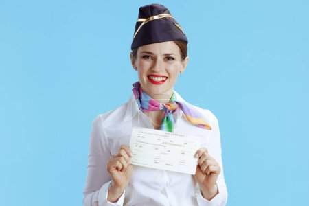 Foto de Sonriente elegante azafata femenina sobre fondo azul en uniforme con billetes de avión. - Imagen libre de derechos