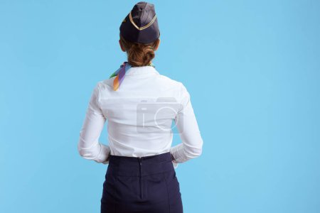 Téléchargez les photos : Vu de derrière hôtesse de l'air féminine moderne sur fond bleu en uniforme. - en image libre de droit