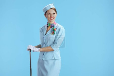 Photo for Happy elegant stewardess woman isolated on blue background in blue uniform with trolley bag looking at copy space. - Royalty Free Image