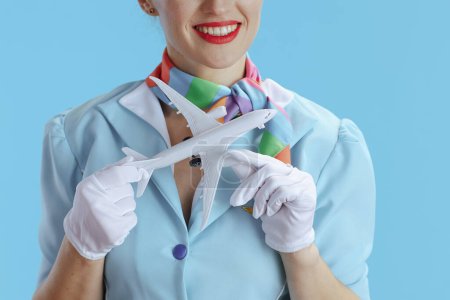 Téléchargez les photos : Gros plan sur une hôtesse de l'air élégante et souriante sur fond bleu en uniforme bleu avec un petit avion. - en image libre de droit