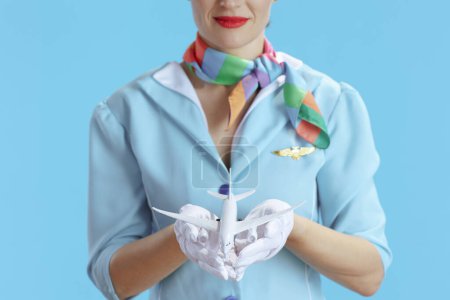 Photo for Closeup on stewardess woman against blue background in blue uniform with a little airplane. - Royalty Free Image