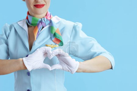 Téléchargez les photos : Gros plan sur élégante hôtesse de l'air femme sur fond bleu uniforme bleu montrant les mains en forme de coeur. - en image libre de droit