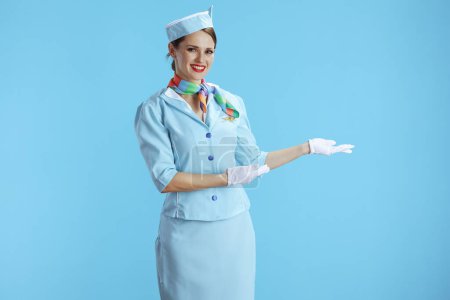 Foto de Feliz mujer auxiliar de vuelo moderno aislado sobre fondo azul en uniforme azul bienvenida. - Imagen libre de derechos