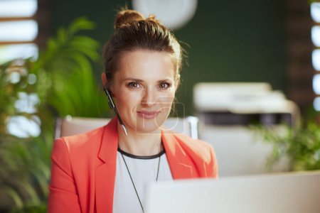 Photo for Sustainable workplace. Portrait of modern business woman at work in a red jacket with headset and laptop. - Royalty Free Image