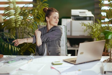 Téléchargez les photos : Un lieu de travail durable. heureuse femme d'affaires moderne au travail avec ordinateur portable étirant les mains. - en image libre de droit