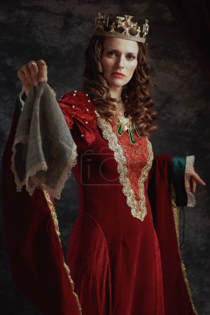 Photo for Medieval queen in red dress with handkerchief and crown on dark gray background. - Royalty Free Image