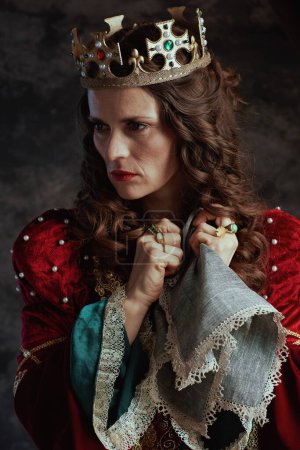 Photo for Pensive medieval queen in red dress with handkerchief and crown on dark gray background. - Royalty Free Image