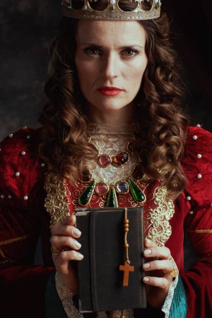 Photo for Medieval queen in red dress with book, rosary and crown on dark gray background. - Royalty Free Image
