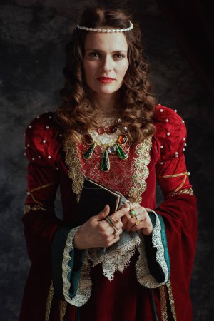 Téléchargez les photos : Reine médiévale en robe rouge avec livre et mouchoir sur fond gris foncé. - en image libre de droit