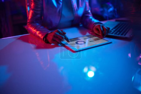 Photo for Neon metaverse futuristic concept. Closeup on middle aged woman with tablet PC and laptop working with charts in office. - Royalty Free Image