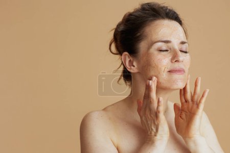 Foto de Mujer moderna con exfoliante facial sobre fondo beige. - Imagen libre de derechos