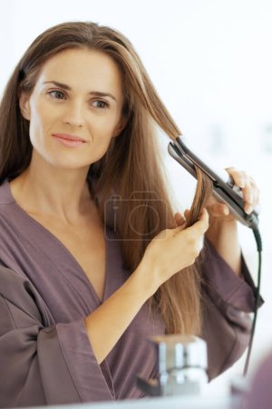 Foto de Mujer joven alisando el cabello en el baño - Imagen libre de derechos
