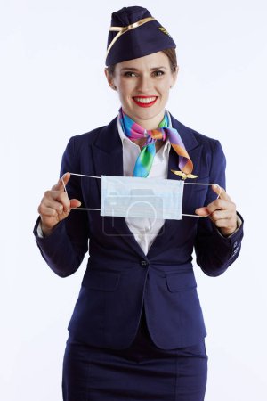 Photo for Happy elegant flight attendant woman against white background in uniform with medical mask. - Royalty Free Image