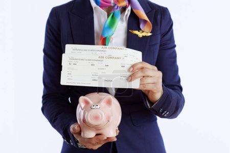 Photo for Closeup on modern female stewardess against white background in uniform with flight tickets and piggy bank. - Royalty Free Image