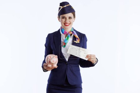 Photo for Happy modern female air hostess isolated on white background in uniform with flight tickets and piggy bank. - Royalty Free Image