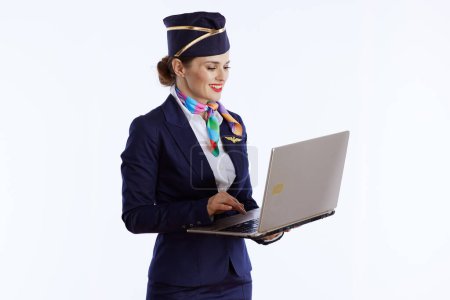 Photo for Happy elegant flight attendant woman against white background in uniform using laptop. - Royalty Free Image