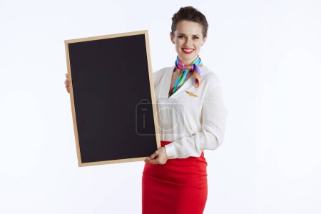 Photo for Smiling elegant flight attendant woman isolated on white background in uniform showing blank board. - Royalty Free Image