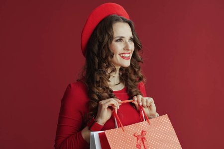 Photo for Happy Valentine. happy elegant woman with long wavy hair in red dress and beret against red background with shopping bags. - Royalty Free Image