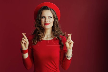 Foto de Feliz San Valentín. mujer de mediana edad elegante excitada con el pelo ondulado largo en vestido rojo y boina sobre fondo rojo con los dedos cruzados. - Imagen libre de derechos