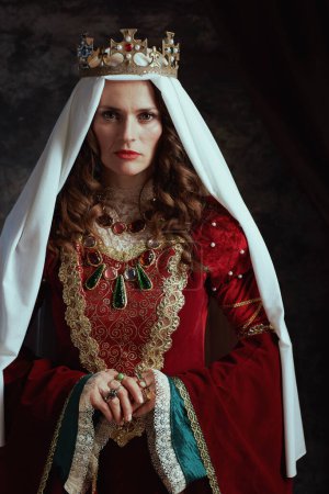 Photo for Medieval queen in red dress with veil and crown on dark gray background. - Royalty Free Image