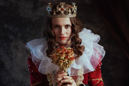 Photo for Medieval queen in red dress with dried flower, white collar and crown on dark gray background. - Royalty Free Image