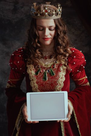 Foto de Reina medieval en vestido rojo con pantalla en blanco tableta digital corona sobre fondo gris oscuro. - Imagen libre de derechos