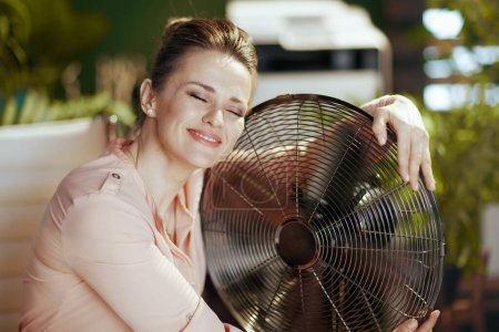 Photo for Sustainable workplace. smiling modern accountant woman in modern green office with electric fan. - Royalty Free Image
