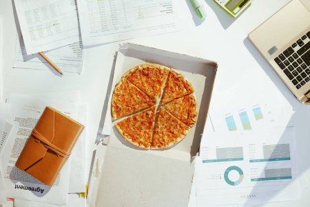 Photo for Upper view of pizza at the table with documents and laptop. - Royalty Free Image