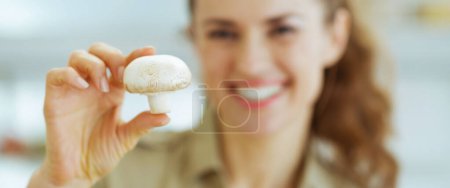 Photo for Smiling young housewife holding mushroom in kitchen - Royalty Free Image