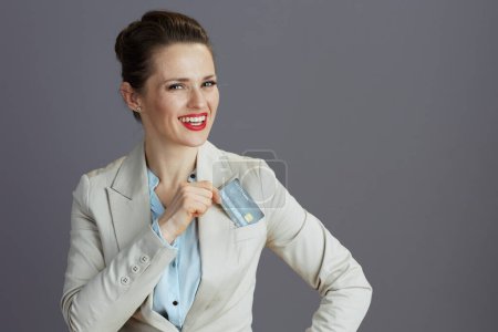 Foto de Feliz elegante 40 años de edad mujer de negocios en un traje de negocios ligero con tarjeta de crédito sobre fondo gris. - Imagen libre de derechos