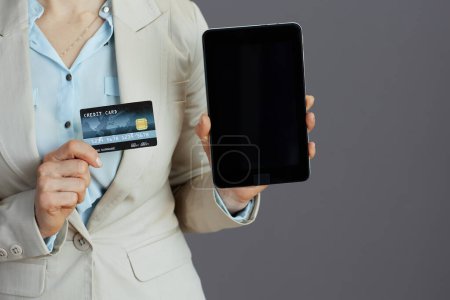 Foto de Primer plano de la mujer propietaria de una pequeña empresa en un traje de negocios ligero con tableta PC y tarjeta de crédito aislada en gris. - Imagen libre de derechos