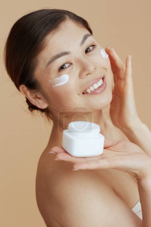 Téléchargez les photos : Moderne asiatique femme avec visage crème pot et visage crème sur visage isolé sur beige fond. - en image libre de droit