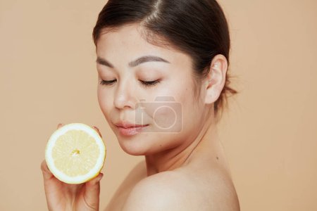 Téléchargez les photos : Détendue jeune asiatique femme avec citron sur fond beige. - en image libre de droit