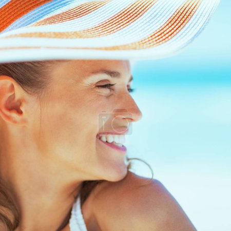Téléchargez les photos : Souriant jeune femme en chapeau sur la plage regardant sur l'espace de copie - en image libre de droit
