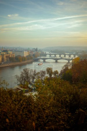 Foto de Paisaje con el río Moldava y el puente de Carlos al atardecer atravesado por el follaje en otoño en Praga, República Checa. - Imagen libre de derechos