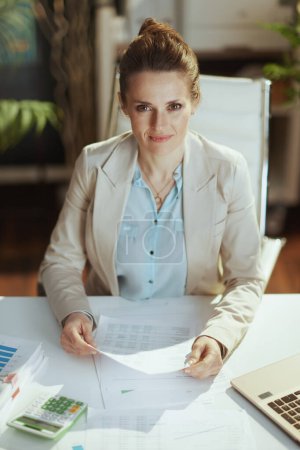 Photo for Portrait of modern middle aged woman employee in a light business suit in modern green office with documents. - Royalty Free Image
