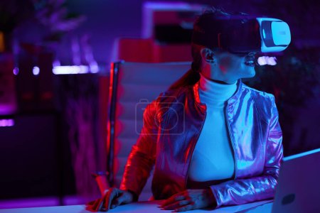 Foto de Neon metaverse futuristic concept. modern 40 years old woman in virtual reality goggles in modern office. - Imagen libre de derechos