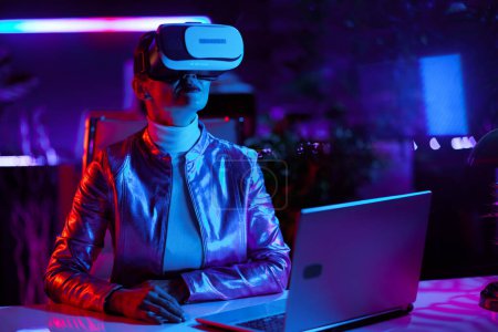 Téléchargez les photos : Neon metaverse concept futuriste. mode 40 ans femme en réalité virtuelle lunettes dans le bureau moderne. - en image libre de droit